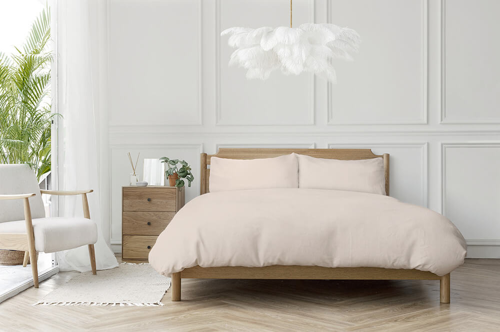 A chandelier of ostrich feathers appears to float above a simple bed dressed in neutral colors.
